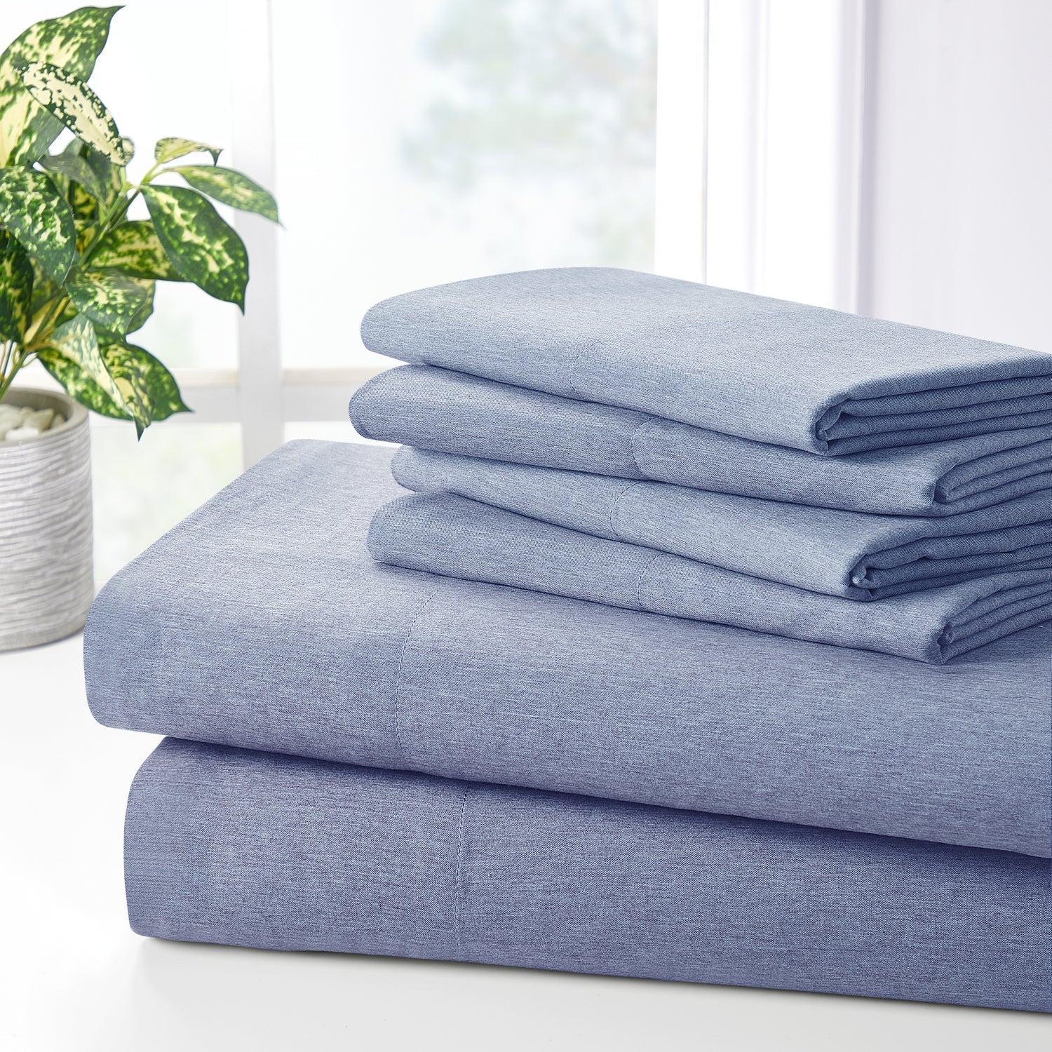 Stack of blue denim fabric on a white surface with a plant in the background