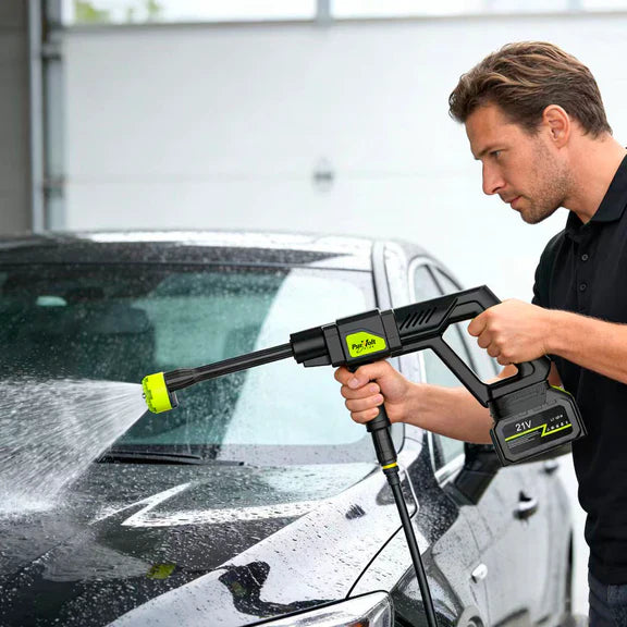 Man using a pressure washer to clean a car in a garage.