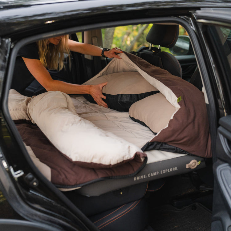 Someone sets up a Luno® Packable Camping Pillow and bedding in their car’s back seat, creating a cozy sleep area with a mattress designed to fit the vehicle’s interior.