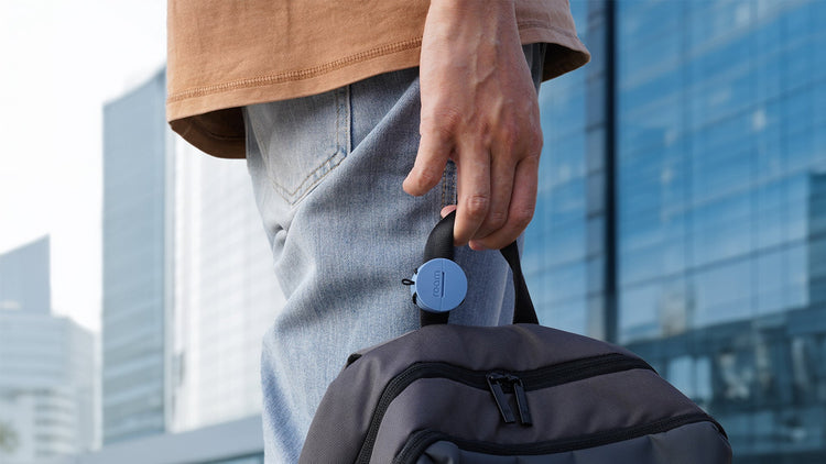 Person holding a backpack with a blurred cityscape in the background