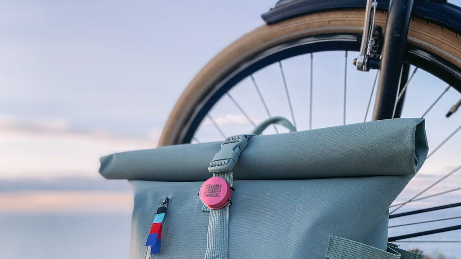 Green roll-top bag attached to a bicycle with a blurred natural background