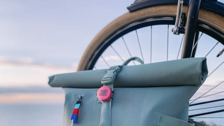 Green roll-top bag attached to a bicycle with a blurred natural background