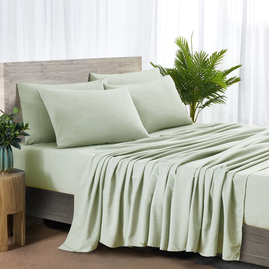 Green bed sheets and pillows on a bed with a wooden headboard and plant in the background.