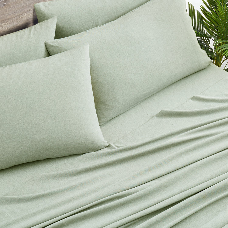 Light green bedding set with pillows on a bed, featuring a natural background.