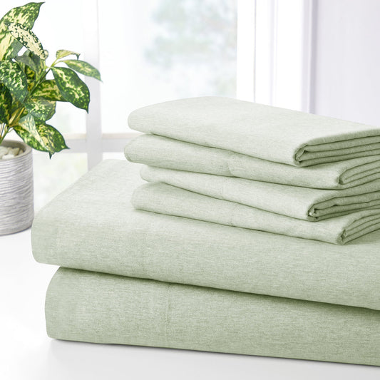 Green bed sheets and pillows on a bed with a wooden headboard and plant in the background.