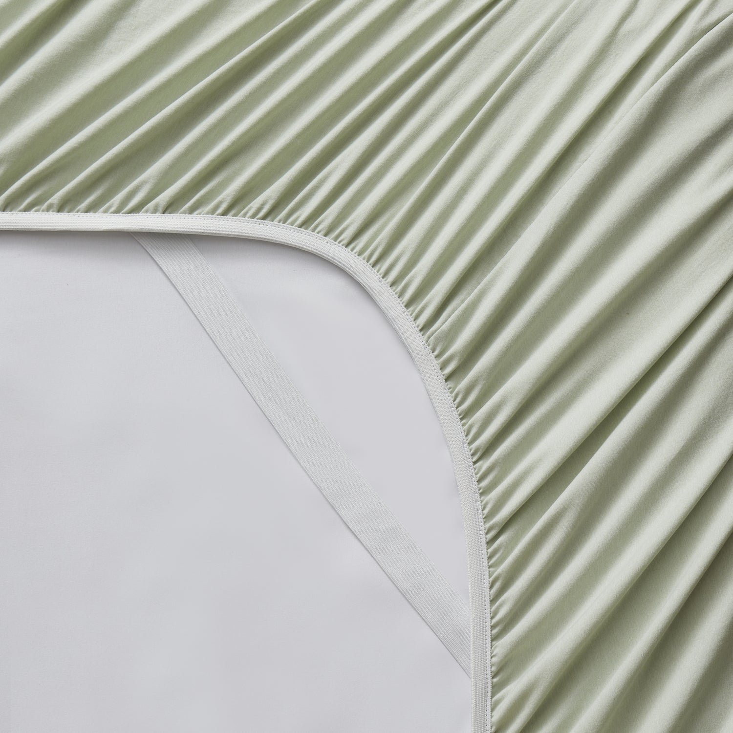 Close-up of a green fitted sheet on a bed with a white mattress.