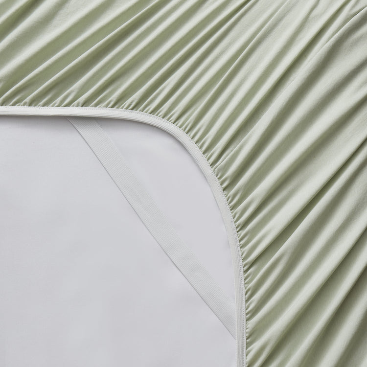 Close-up of a green fitted sheet on a bed with a white mattress.