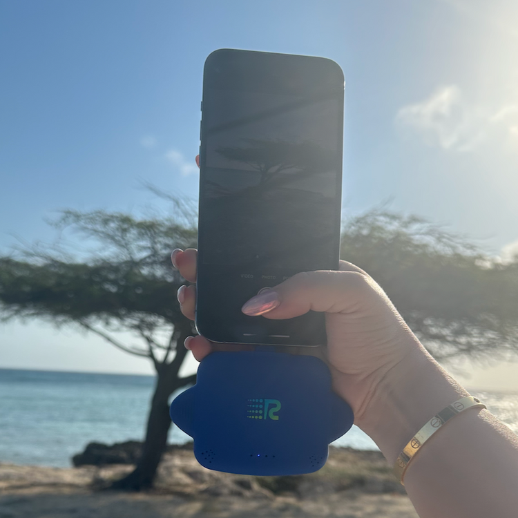 Hand holding a phone with a blue case on a beach