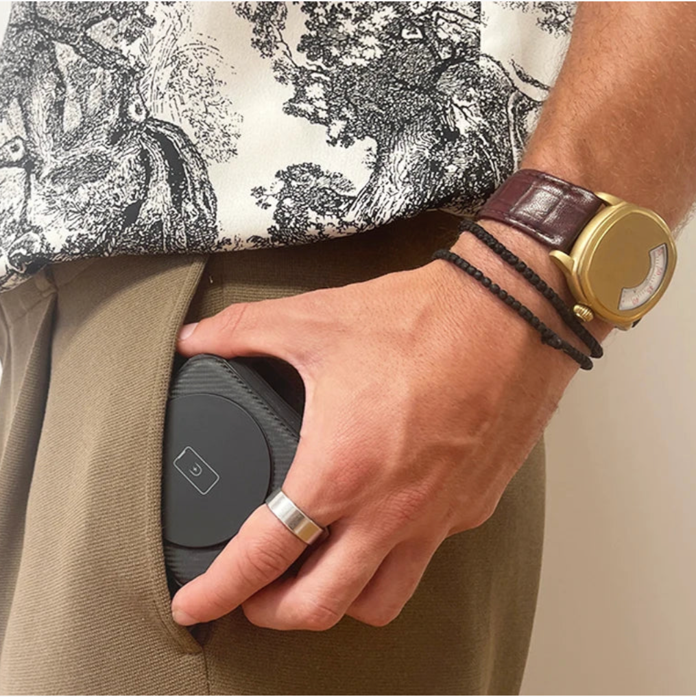 Person holding a black wireless charging pad with a gold watch on wrist