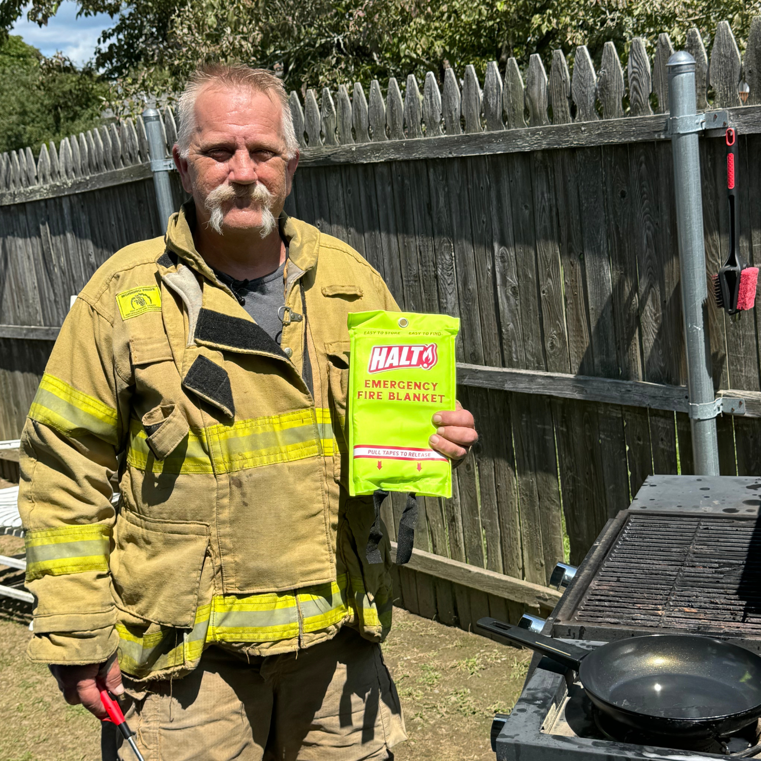 Man in firefighter uniform holding a Halti emergency fire blanket outdoors.