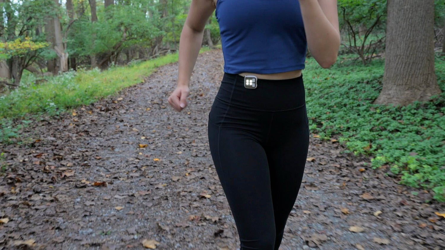 Person wearing a blue top and black leggings walking on a path in a forest.