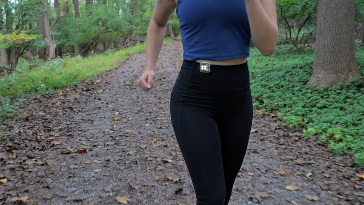Person wearing a blue top and black leggings walking on a path in a forest.