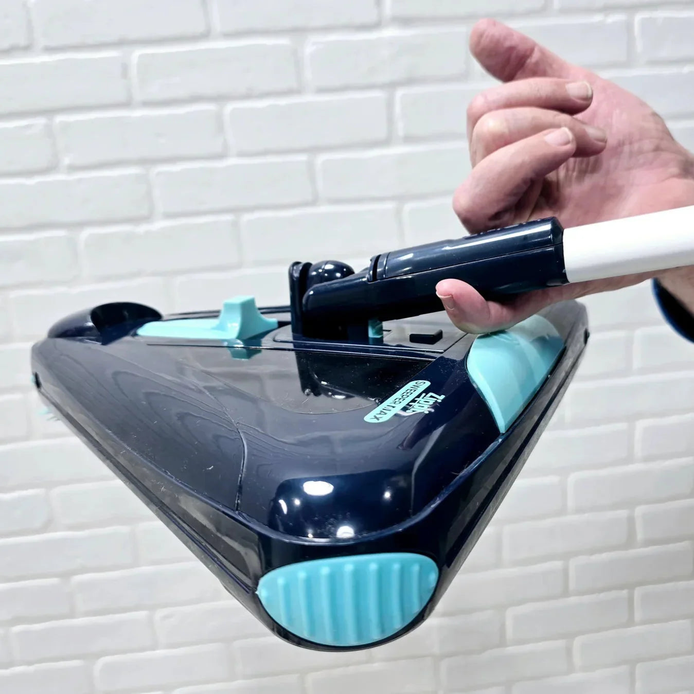 Person using a handheld cleaning device against a white brick wall.