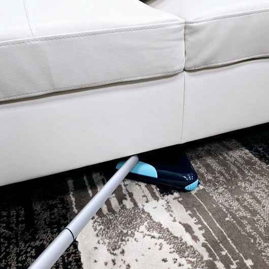Cleaning tool under a white sofa on a patterned carpet