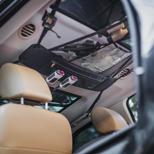 Interior view of an adventure mobile showcasing a Luno® Cargo Hammock attached to the ceiling above the back seats. Various items such as tools and small bags are stored on the portable gear shelf, maximizing storage space. The rear seats and part of the front seats are visible.