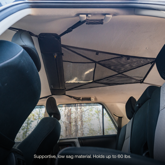 Interior view of an adventure mobile showcasing a Luno® Cargo Hammock attached to the ceiling above the back seats. Various items such as tools and small bags are stored on the portable gear shelf, maximizing storage space. The rear seats and part of the front seats are visible.