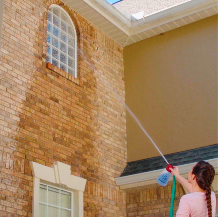 Person cleaning a brick building with a pressure washer