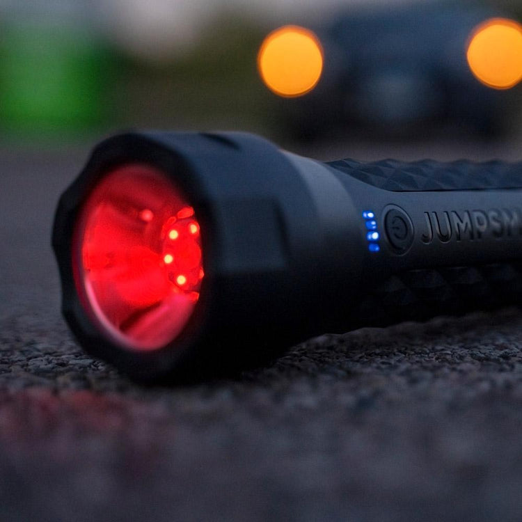 Black flashlight with red light on a textured surface, blurred lights in the background
