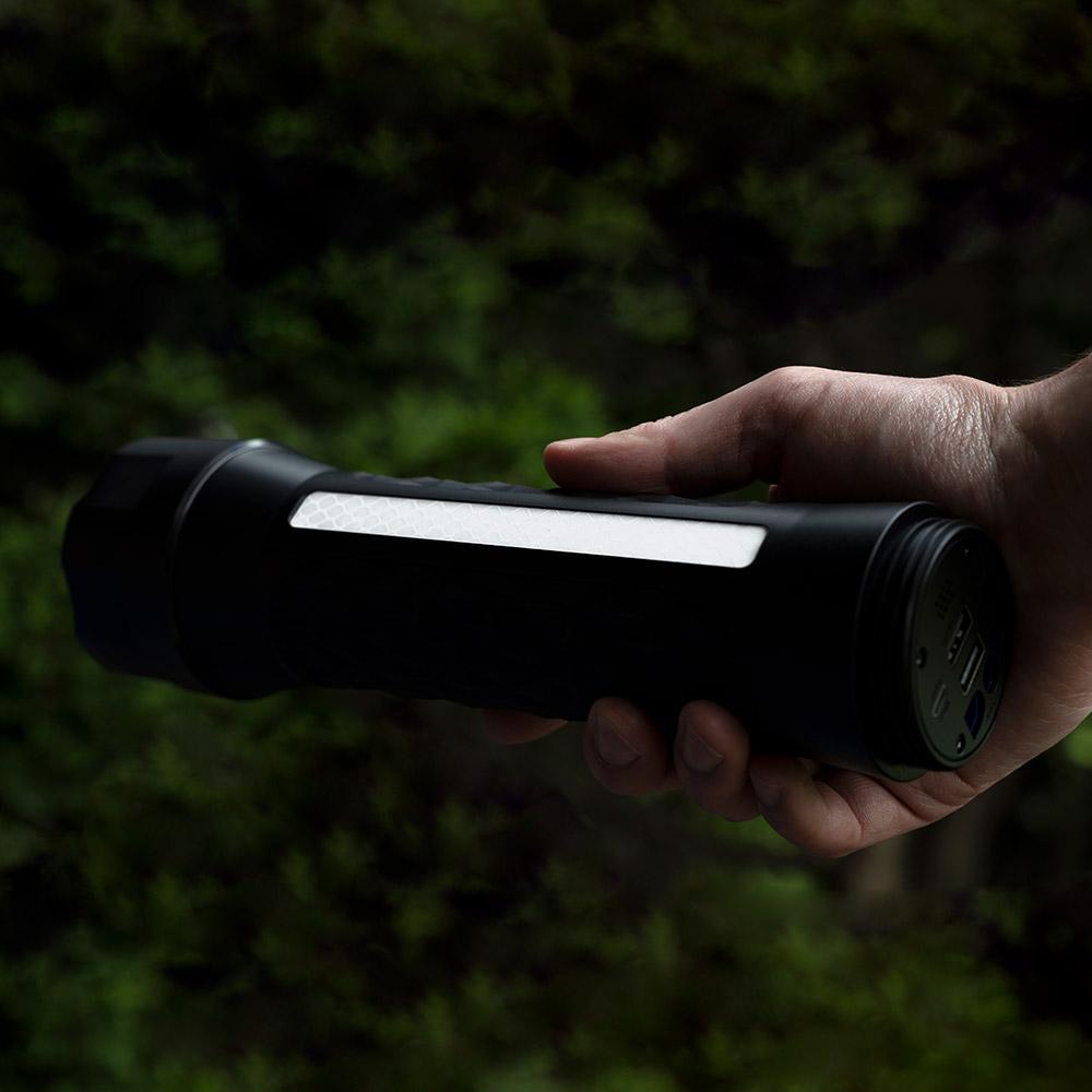 Hand holding a black flashlight with a light on against a dark background