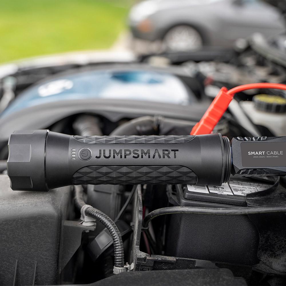 Jumpstart device labeled 'Jumpsmart' on a car engine with a blurred background