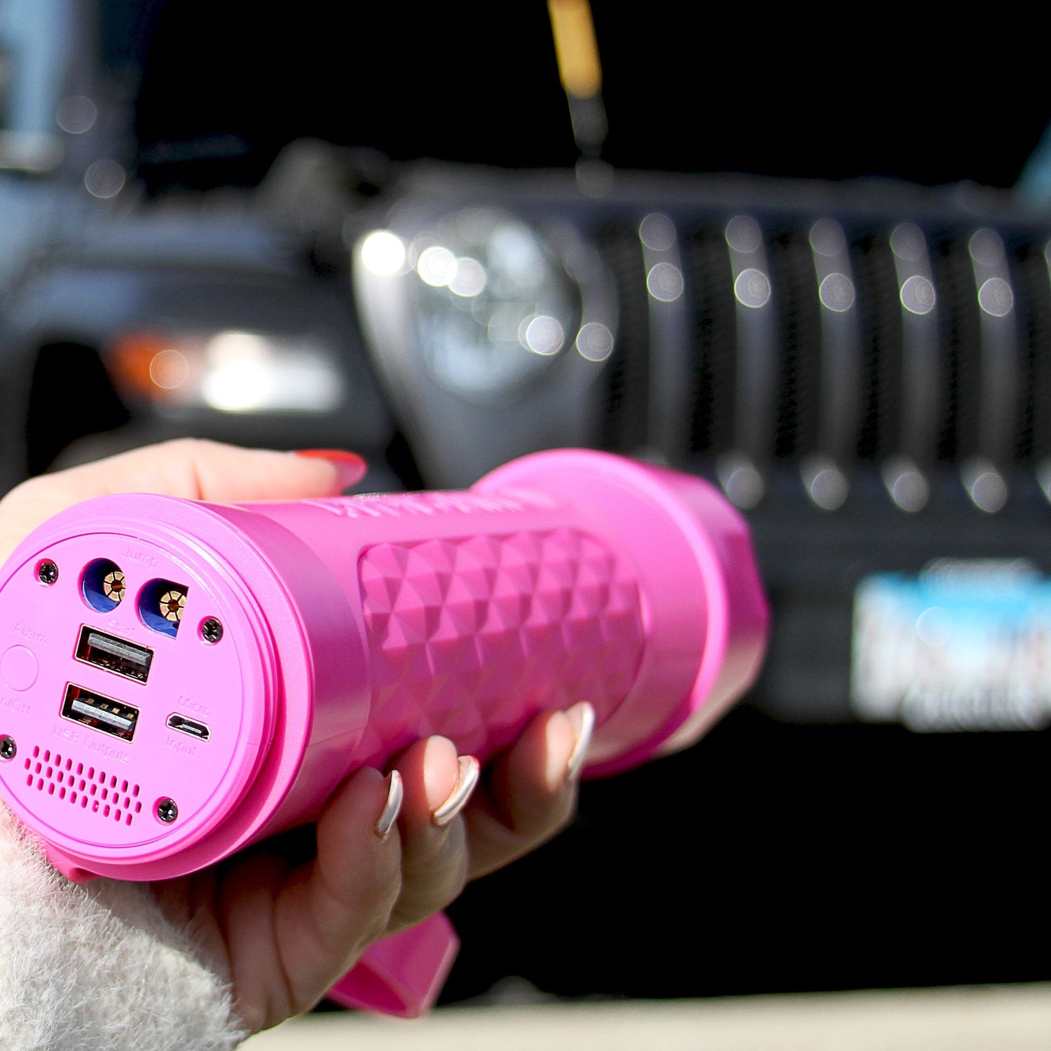 Pink portable device with USB ports held in front of a Jeep vehicle
