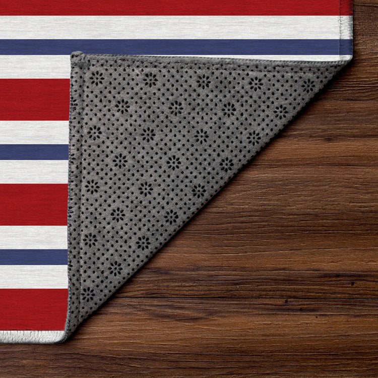 Gray patterned blanket with paw prints on a wooden surface, partially covering a red, white, and blue striped fabric.