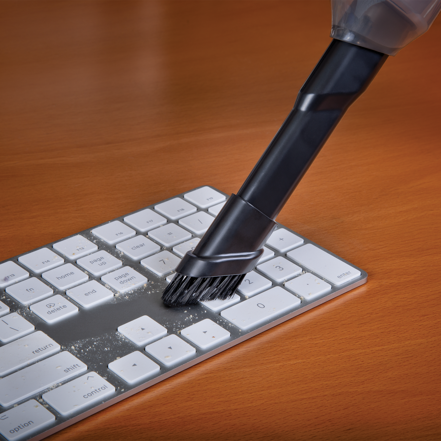 Keyboard cleaning brush cleaning a keyboard on a wooden surface