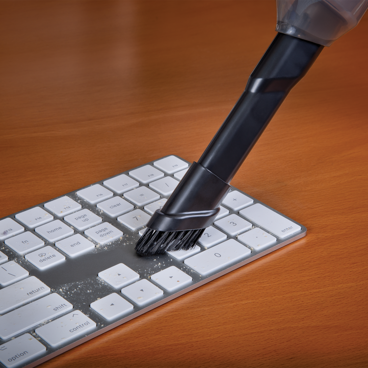 Keyboard cleaning brush cleaning a keyboard on a wooden surface